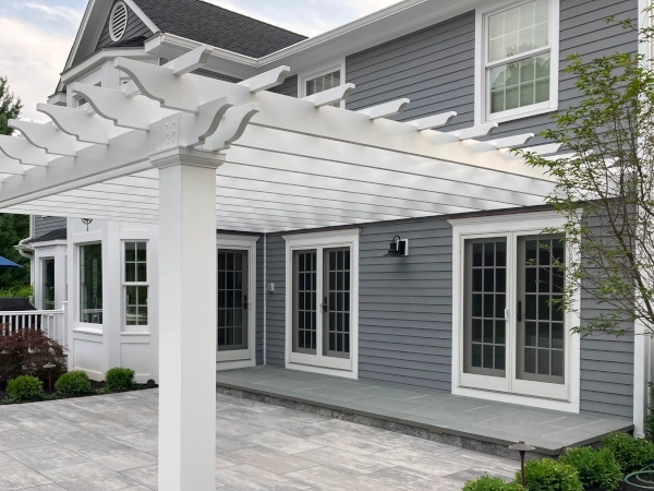 A beautiful white pergola attached to a gray house